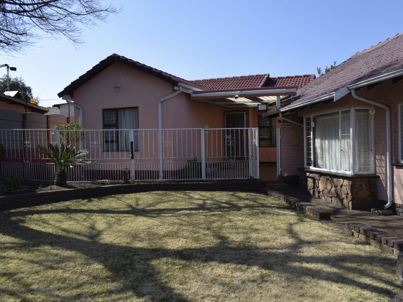 Rear view of the property featuring a paved walkway, covered patio area, and a private garden with stone-clad accents and security fencing.