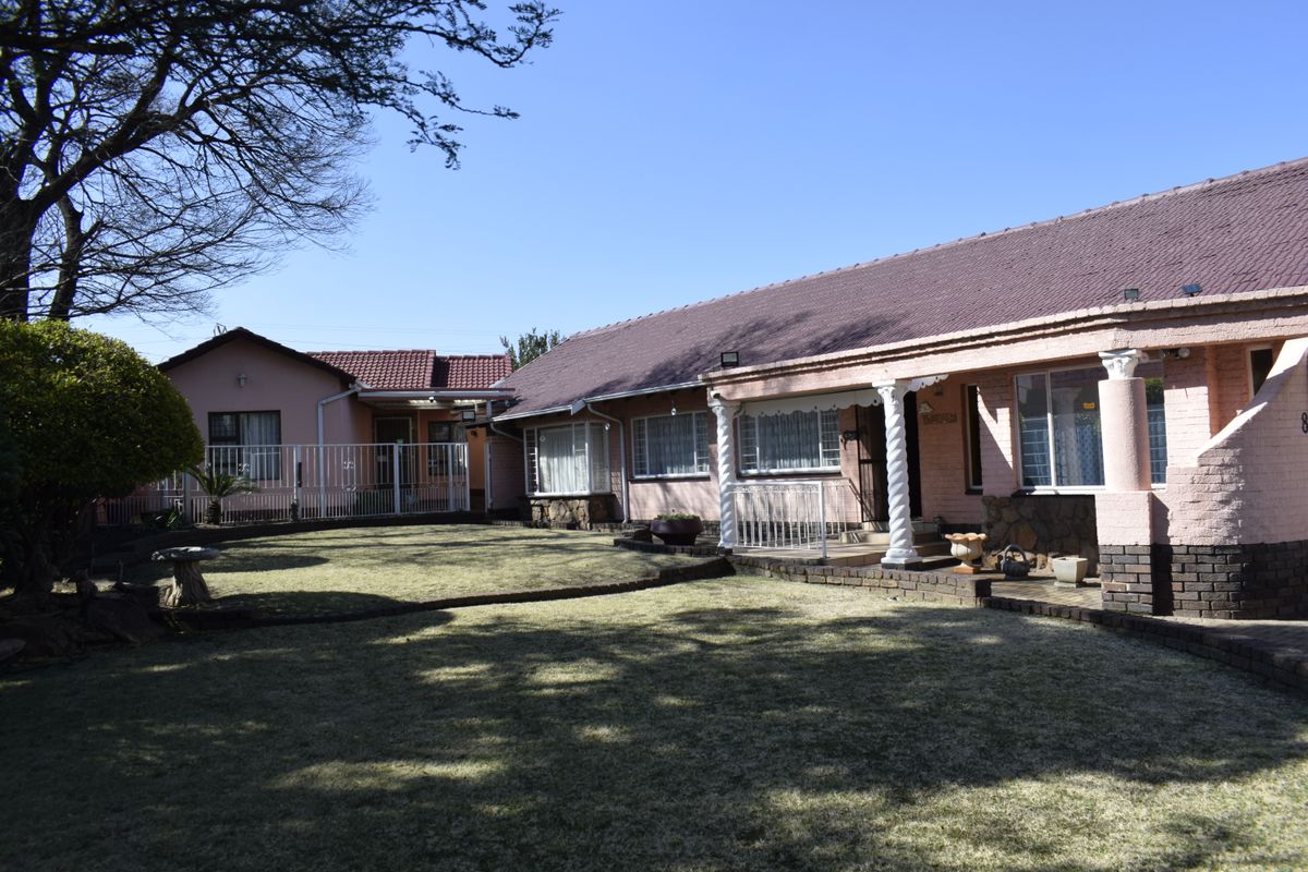 Rear view of a single-story house featuring a tiled roof, brick facade, and a covered patio area overlooking a lawn.