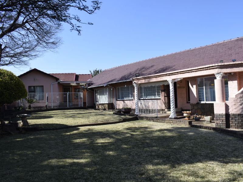 Rear view of a single-story house featuring a tiled roof, brick facade, and a covered patio area overlooking a lawn.