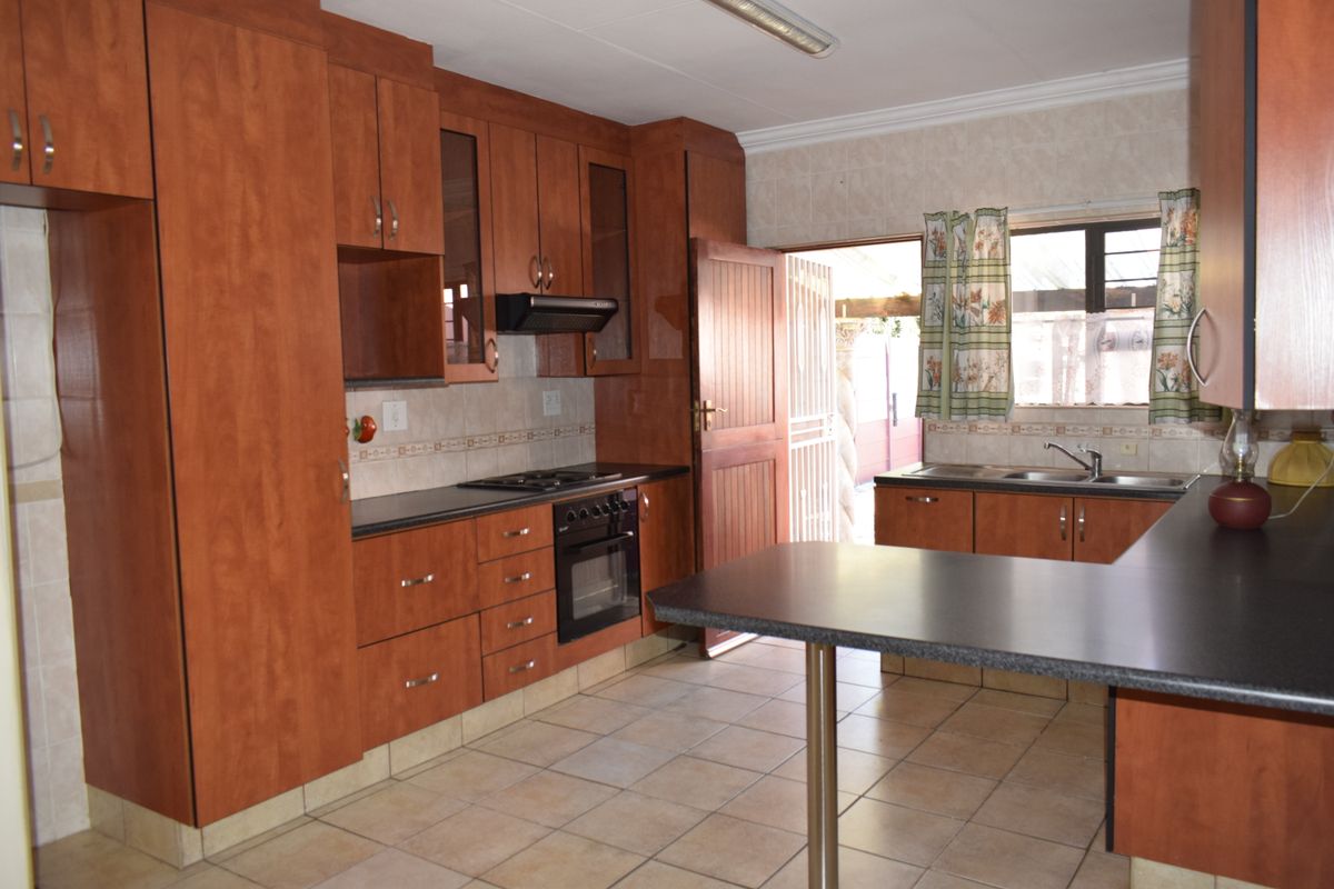 A functional kitchen featuring wood-finish cabinetry, dark laminate countertops, built-in oven with gas hob, and tiled flooring with direct access to the exterior.