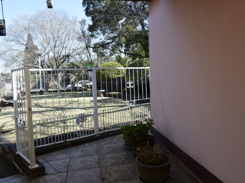 A covered patio area featuring tiled flooring and metal security fencing, overlooking a garden space.