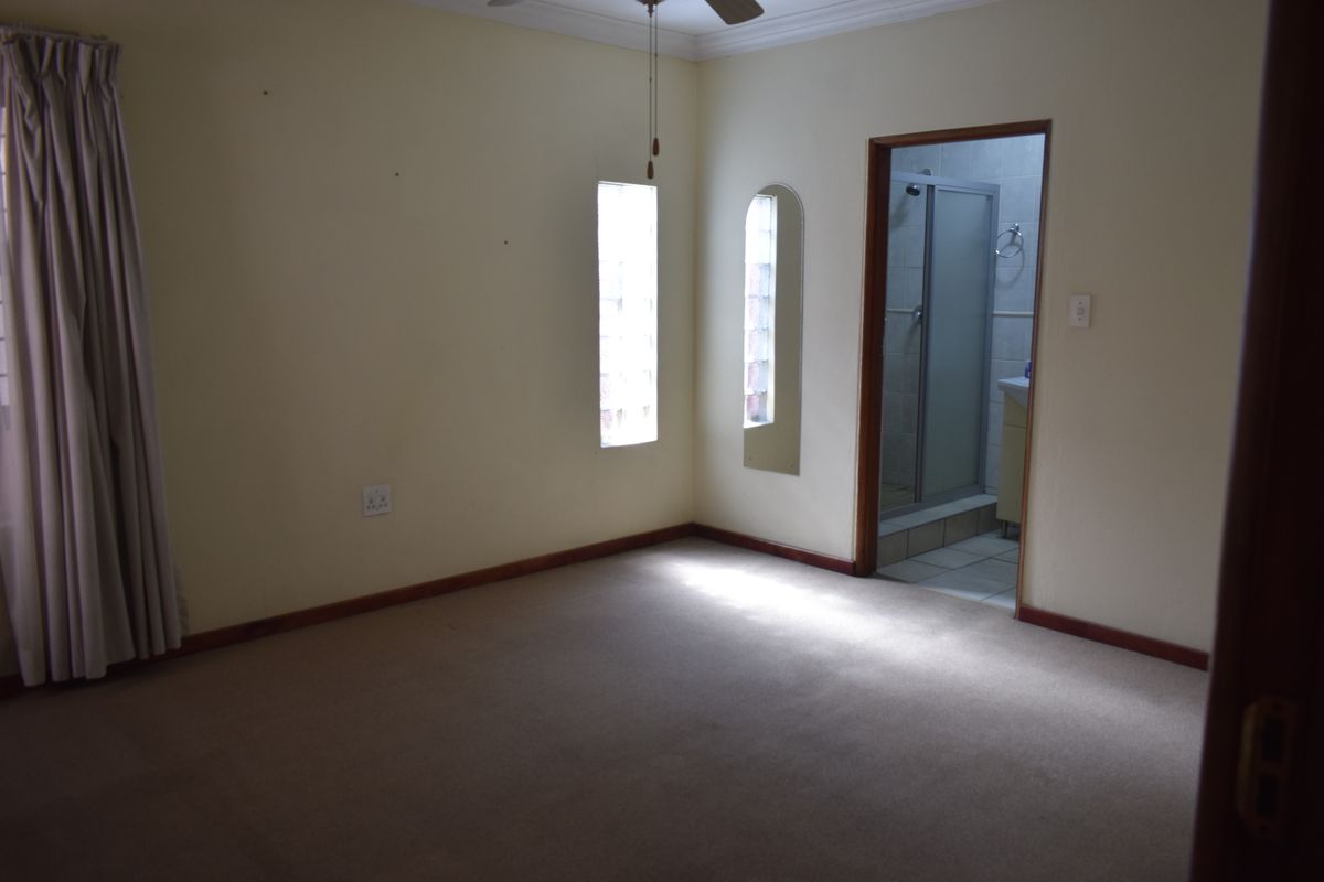 A vacant bedroom featuring carpeted flooring, glass block windows, and direct access to an en-suite bathroom.