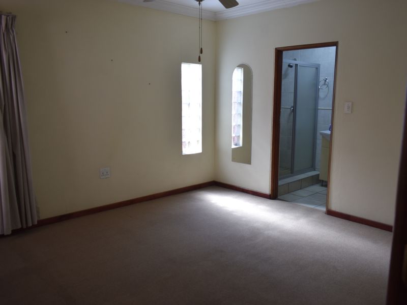 A vacant bedroom featuring carpeted flooring, glass block windows, and direct access to an en-suite bathroom.