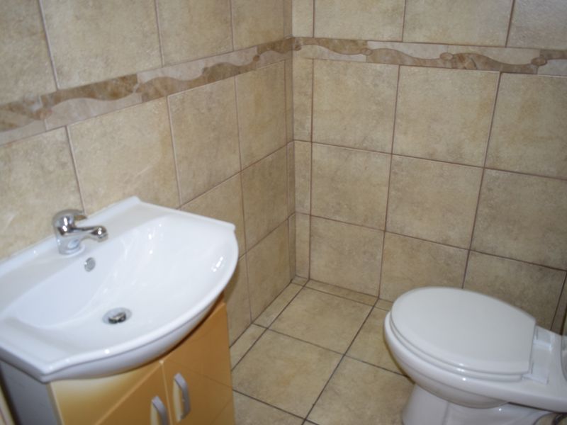 A compact bathroom featuring a vanity basin with a mixer tap, a standard toilet, and full-height ceramic wall tiling.