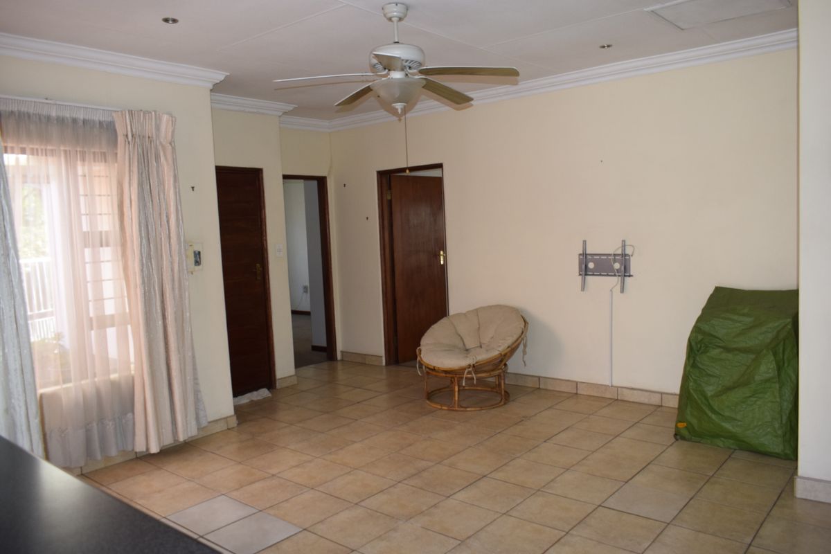 A spacious living area featuring neutral tiled flooring, a ceiling fan, and coved cornicing, offering a blank canvas for interior design.
