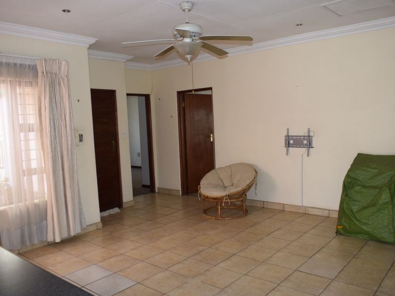 A spacious living area featuring neutral tiled flooring, a ceiling fan, and coved cornicing, offering a blank canvas for interior design.