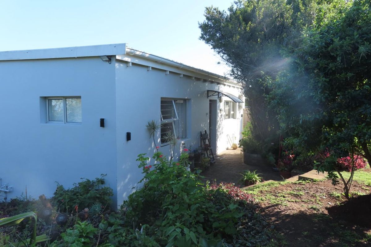 A view of the rear exterior of the house featuring a paved walkway, established garden, and aluminium window frames.