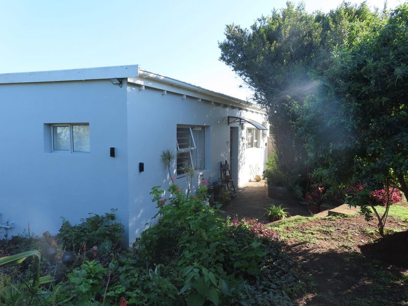 A view of the rear exterior of the house featuring a paved walkway, established garden, and aluminium window frames.