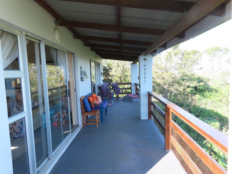 A covered balcony featuring timber structural elements, a wooden balustrade, and sliding glass doors providing access to the interior living space.