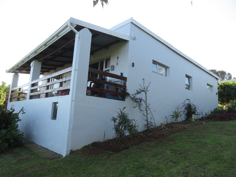 Rear view of the property featuring a covered patio with a timber balustrade and a well-maintained sloped garden area.