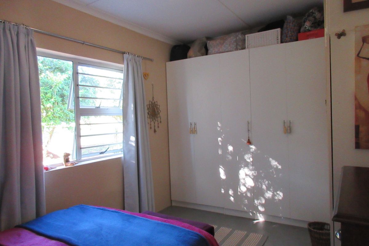 A bedroom featuring built-in cupboards and a window with an aluminium frame, providing natural light and storage space.