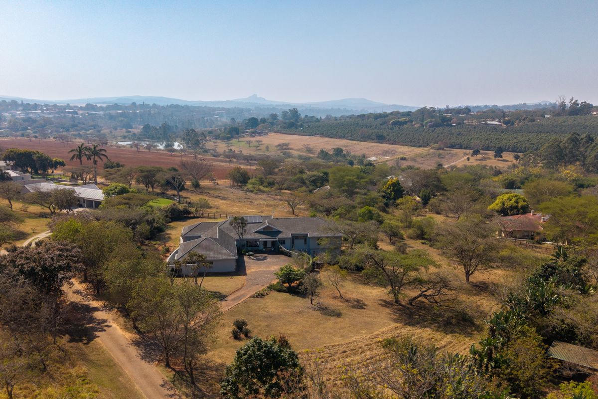 Aerial view of a residential property featuring a tiled roof home, paved driveway, and expansive surrounding grounds in a rural landscape setting.