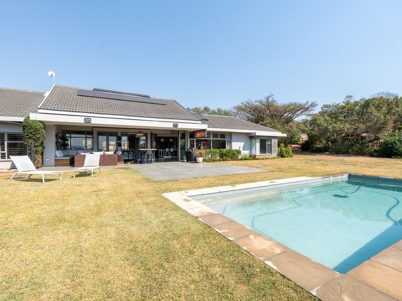 Rear view of the property featuring a swimming pool, paved patio area, and a spacious garden with solar panels installed on the tiled roof.
