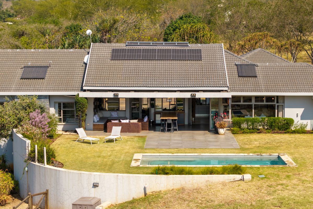 Rear view of the house featuring a tiled roof with solar panels, a swimming pool, paved patio area, and a landscaped garden.
