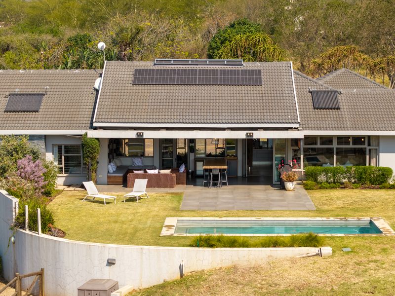 Rear view of the house featuring a tiled roof with solar panels, a swimming pool, paved patio area, and a landscaped garden.