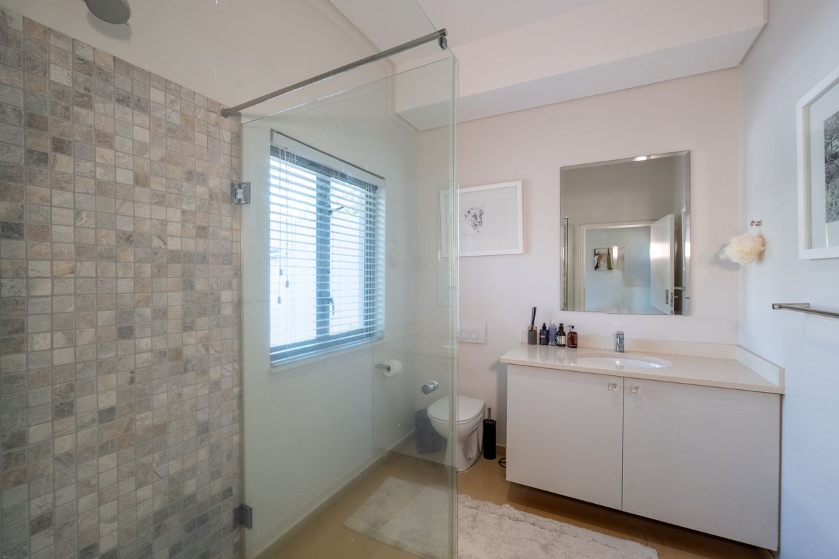 Modern bathroom featuring a glass-enclosed shower with mosaic tiling, a vanity with integrated sink, and a wall-mounted mirror.