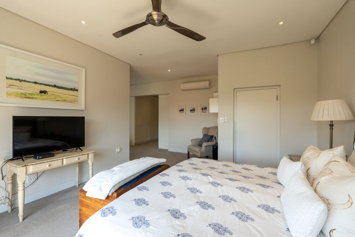 A well-maintained bedroom featuring neutral tones, carpeted flooring, a ceiling fan, and a wall-mounted split-system air conditioner.