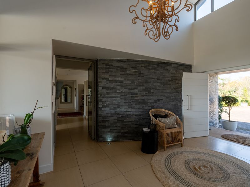 Spacious entrance hall featuring a striking stone feature wall, high ceilings, and large pivot door leading to the exterior.