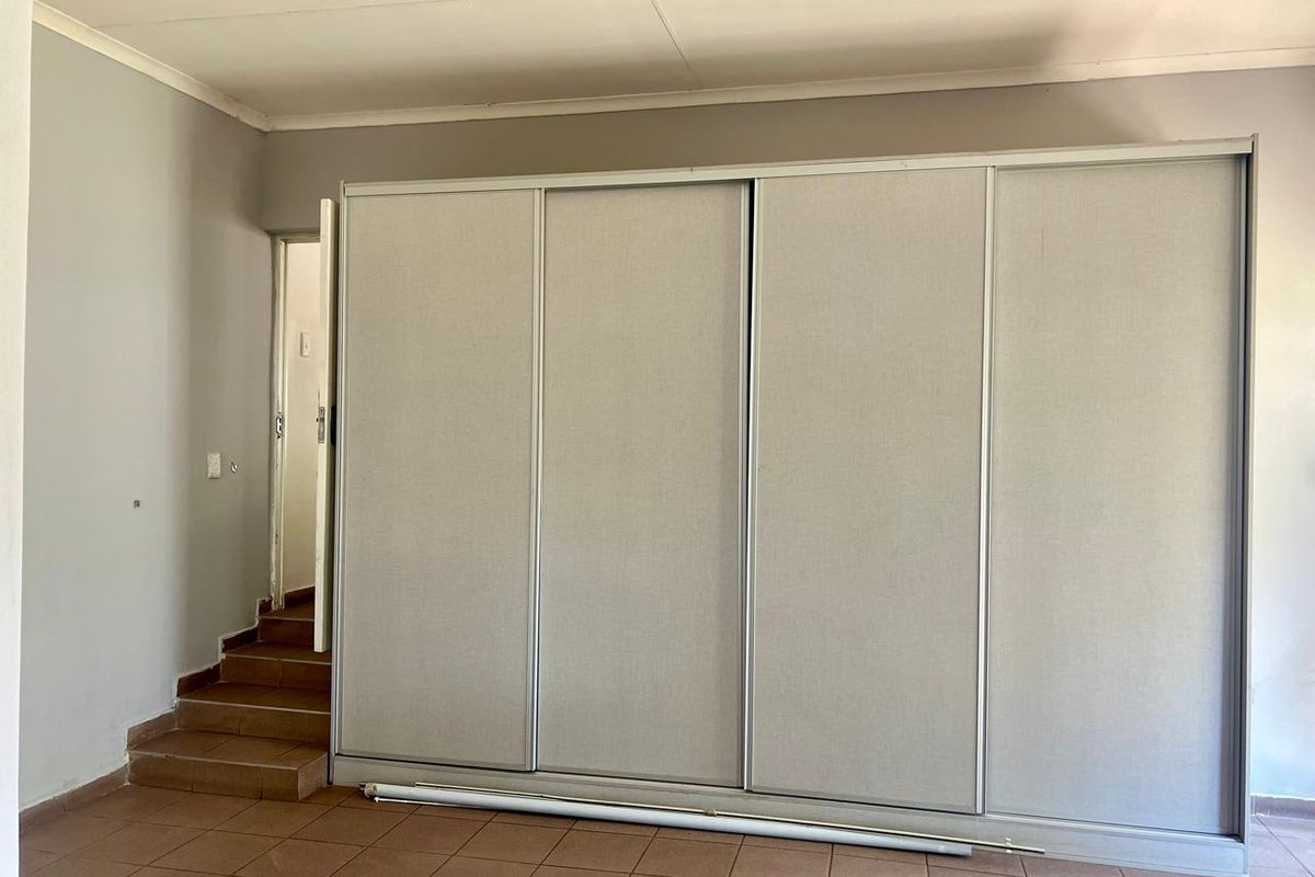 A spacious bedroom featuring a large built-in sliding door wardrobe, tiled flooring, and an internal staircase leading to an adjacent area.