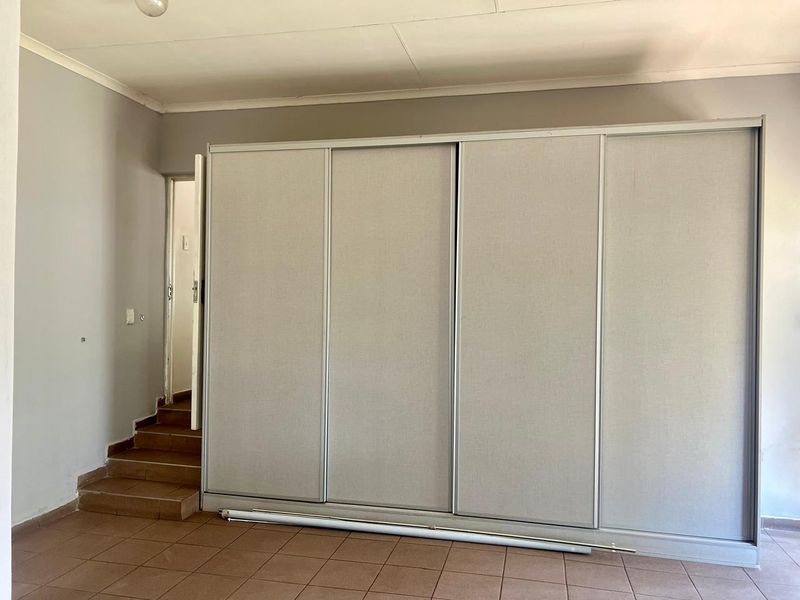 A spacious bedroom featuring a large built-in sliding door wardrobe, tiled flooring, and an internal staircase leading to an adjacent area.
