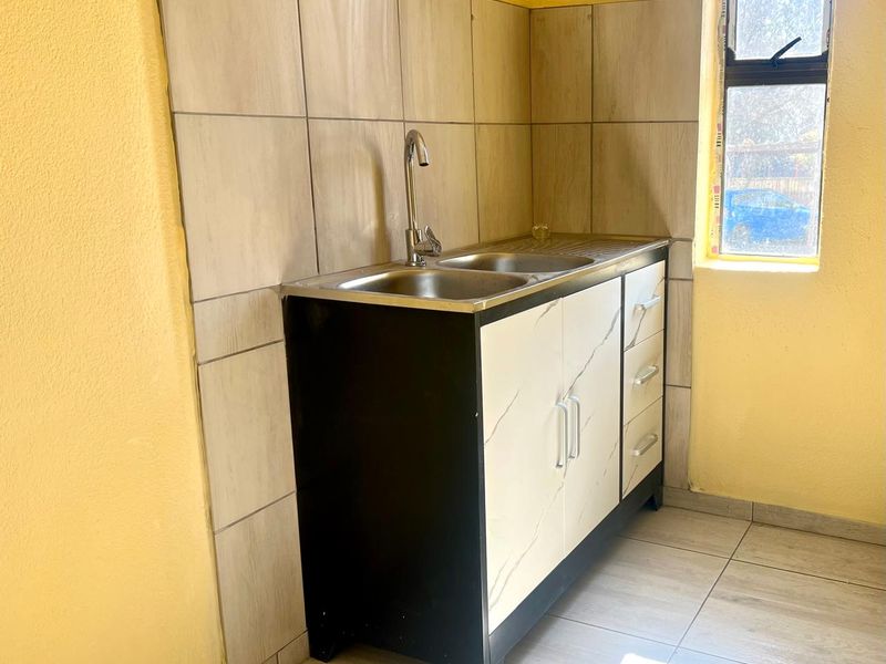 A compact scullery area featuring a stainless steel sink, built-in cabinetry with marble-look doors, and tiled splashback finishes.