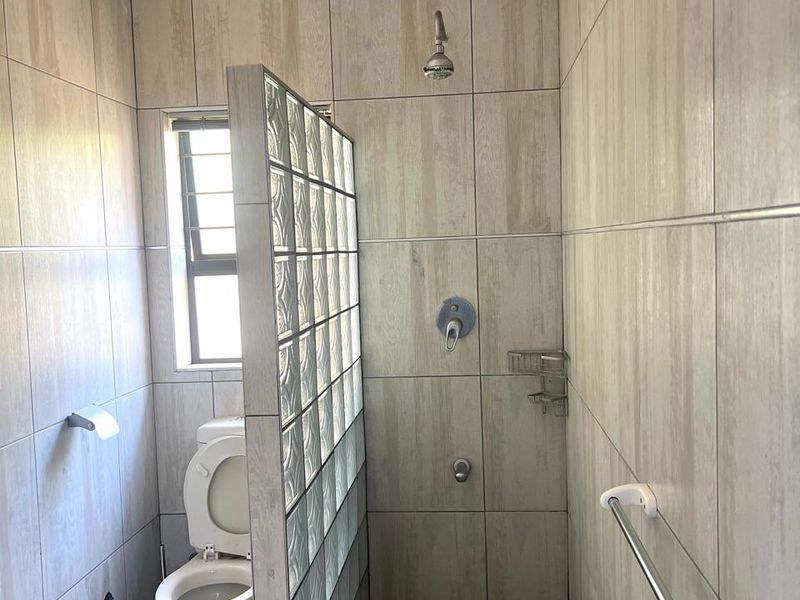 A functional bathroom featuring a glass block shower partition, tiled walls and flooring, and standard sanitary fixtures.