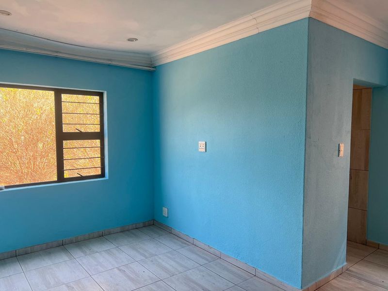 An empty bedroom featuring light blue walls, tiled flooring, and a window with security bars, offering a blank canvas for personalization.