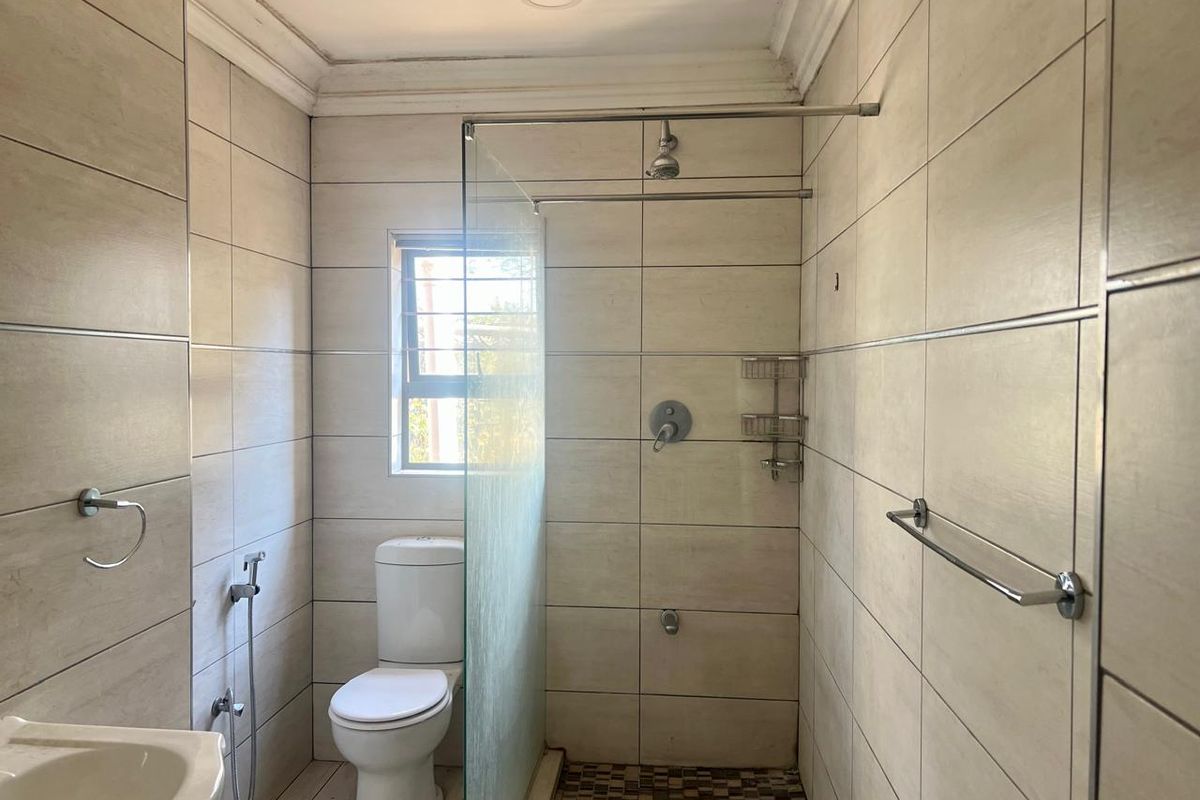 A clean, tiled bathroom featuring a walk-in shower with a glass screen, a modern toilet, and chrome fixtures.
