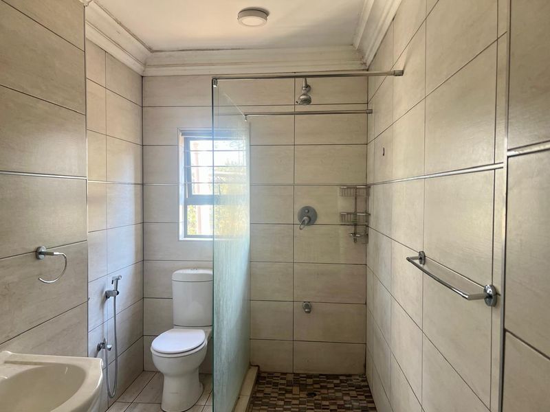 A clean, tiled bathroom featuring a walk-in shower with a glass screen, a modern toilet, and chrome fixtures.