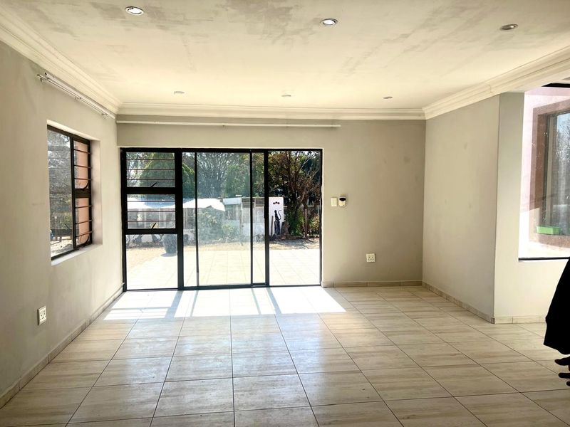 A bright, empty living room featuring tiled flooring, recessed lighting, and large sliding glass doors leading to an outdoor area.