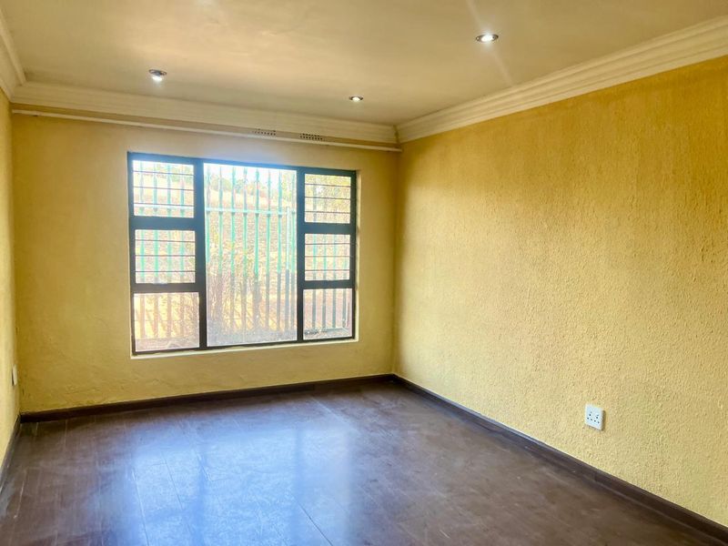 An empty living room featuring laminate flooring, recessed downlighting, and large windows with security bars, finished with textured yellow walls.