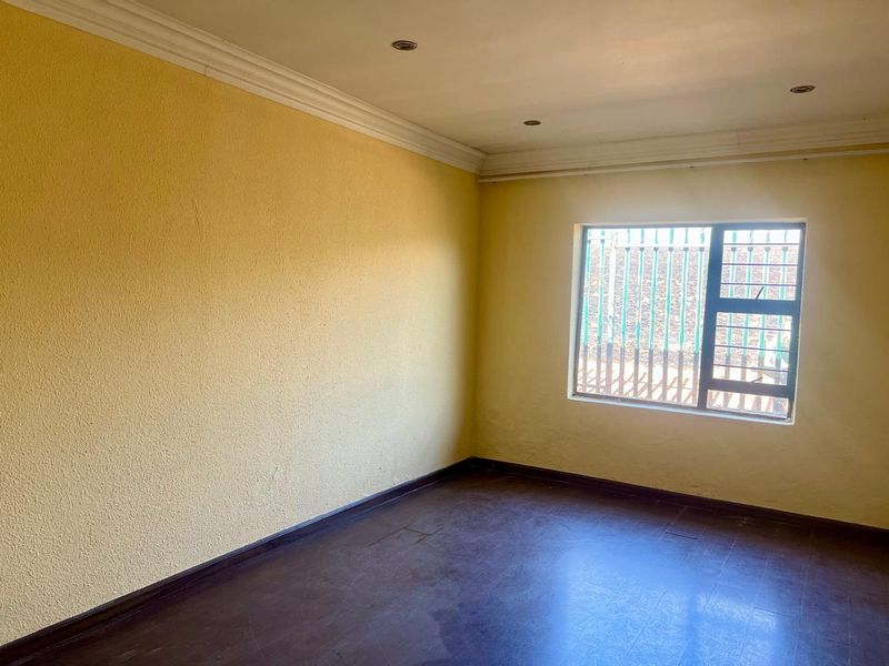 An empty bedroom featuring yellow walls, tiled flooring, recessed ceiling lighting, and a window fitted with security bars.