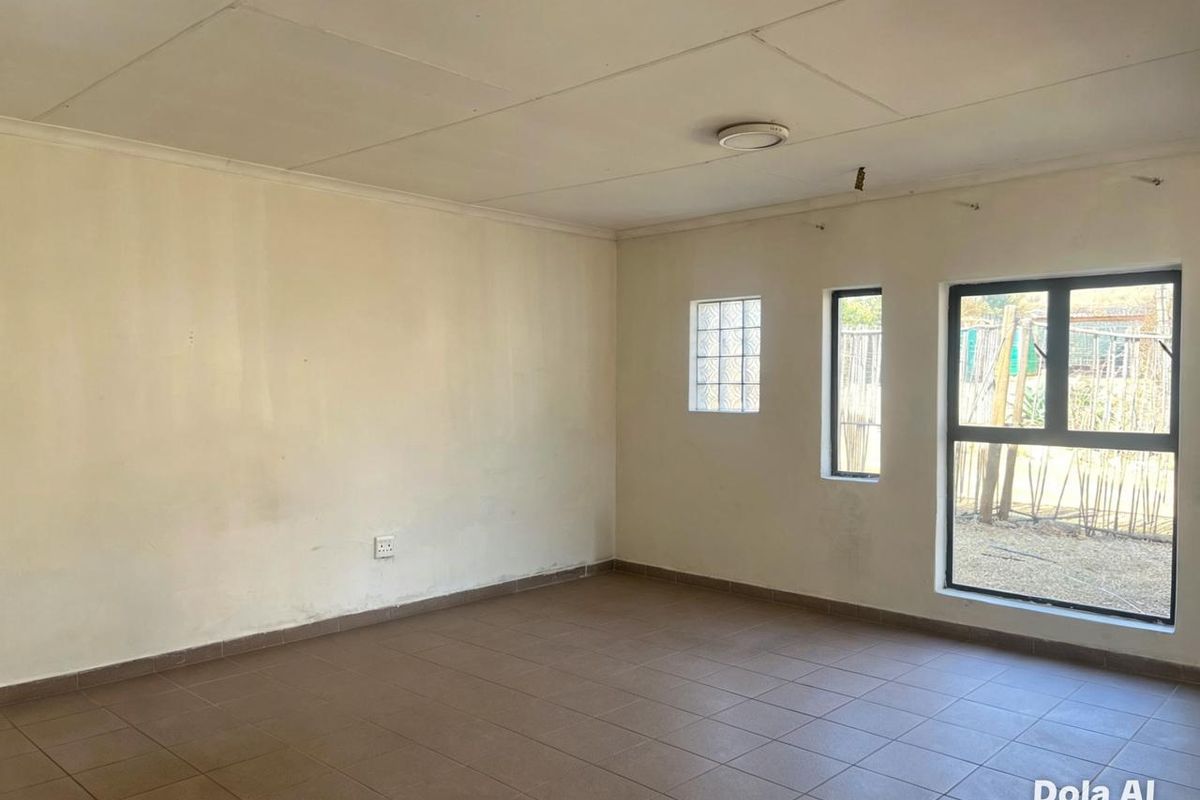 An empty living room featuring tiled flooring, aluminium window frames, and a glass block window, providing a blank canvas for interior design.