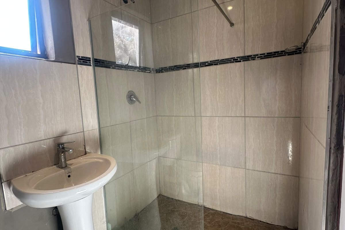 A compact bathroom featuring a pedestal basin, a walk-in shower with a glass screen, and neutral wall tiling.