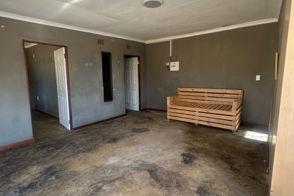 A spacious living area featuring concrete flooring, built-in storage, and multiple doorways, requiring cosmetic updates to improve the overall condition and aesthetic appeal.