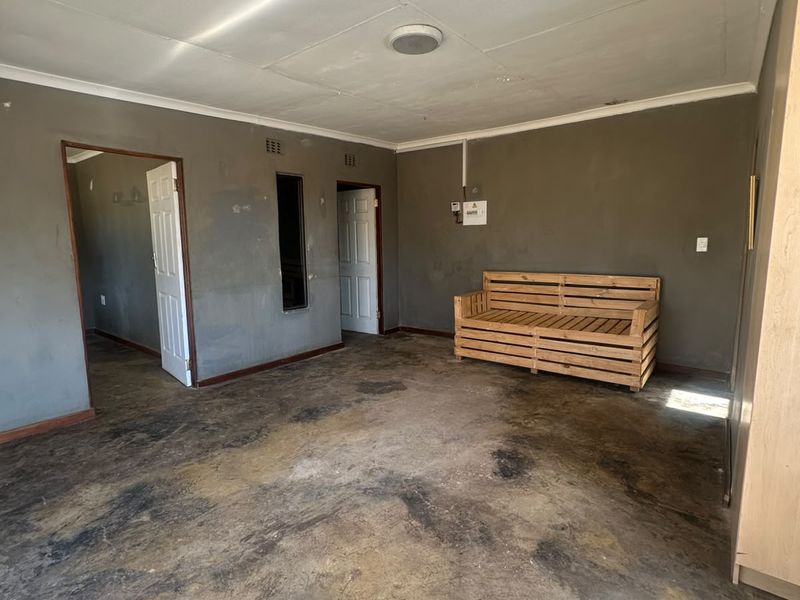 A spacious living area featuring concrete flooring, built-in storage, and multiple doorways, requiring cosmetic updates to improve the overall condition and aesthetic appeal.