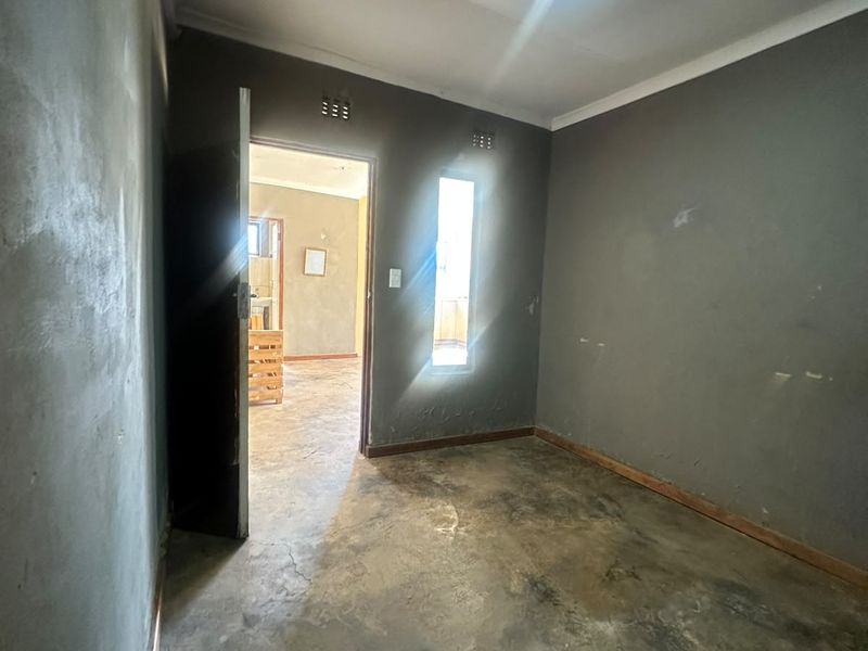 An empty bedroom featuring unfinished grey walls, concrete flooring, and a vertical window, offering a blank canvas for renovation.