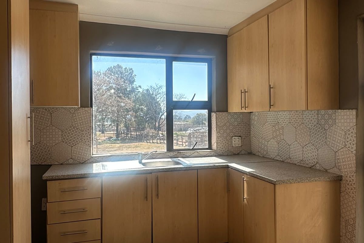 A compact kitchen featuring light wood-finish cabinetry, patterned tile backsplash, and a stainless steel sink, requiring cosmetic updates to the flooring and walls.