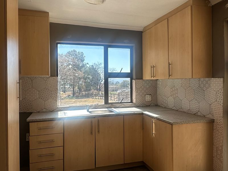 A compact kitchen featuring light wood-finish cabinetry, patterned tile backsplash, and a stainless steel sink, requiring cosmetic updates to the flooring and walls.