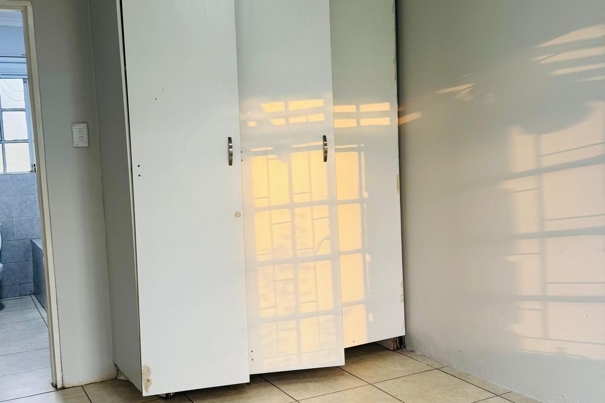 An empty bedroom featuring tiled flooring and a built-in wardrobe with visible wear and tear on the cabinetry.