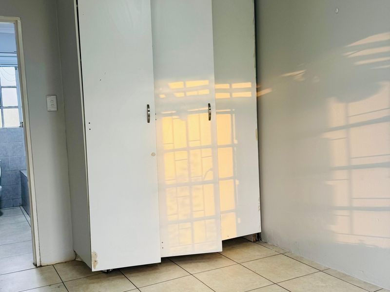 An empty bedroom featuring tiled flooring and a built-in wardrobe with visible wear and tear on the cabinetry.