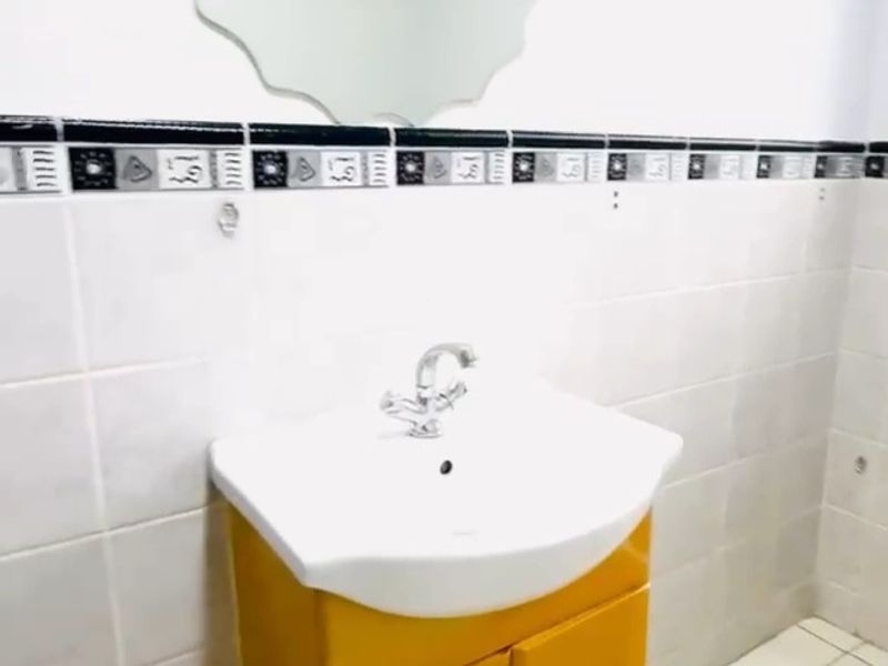 A functional bathroom featuring a vanity cabinet with a ceramic basin, mixer tap, wall mirror, and decorative tiled border.