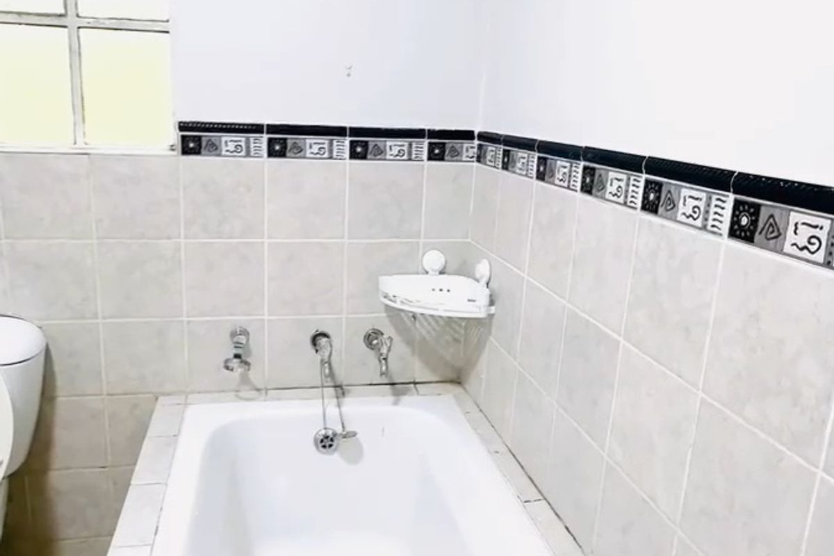 A functional bathroom featuring a built-in bathtub with tiled splashback and decorative border tiles, providing a clean and simple space.