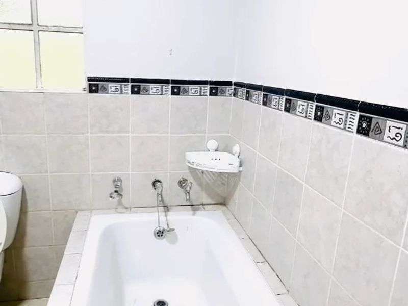 A functional bathroom featuring a built-in bathtub with tiled splashback and decorative border tiles, providing a clean and simple space.