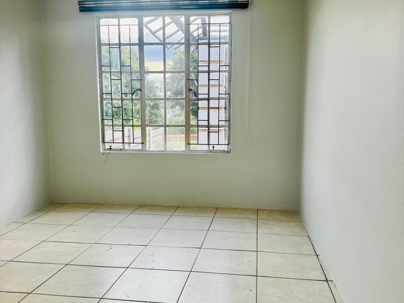 An empty bedroom featuring neutral wall paint, tiled flooring, and a window fitted with security bars and a blind.