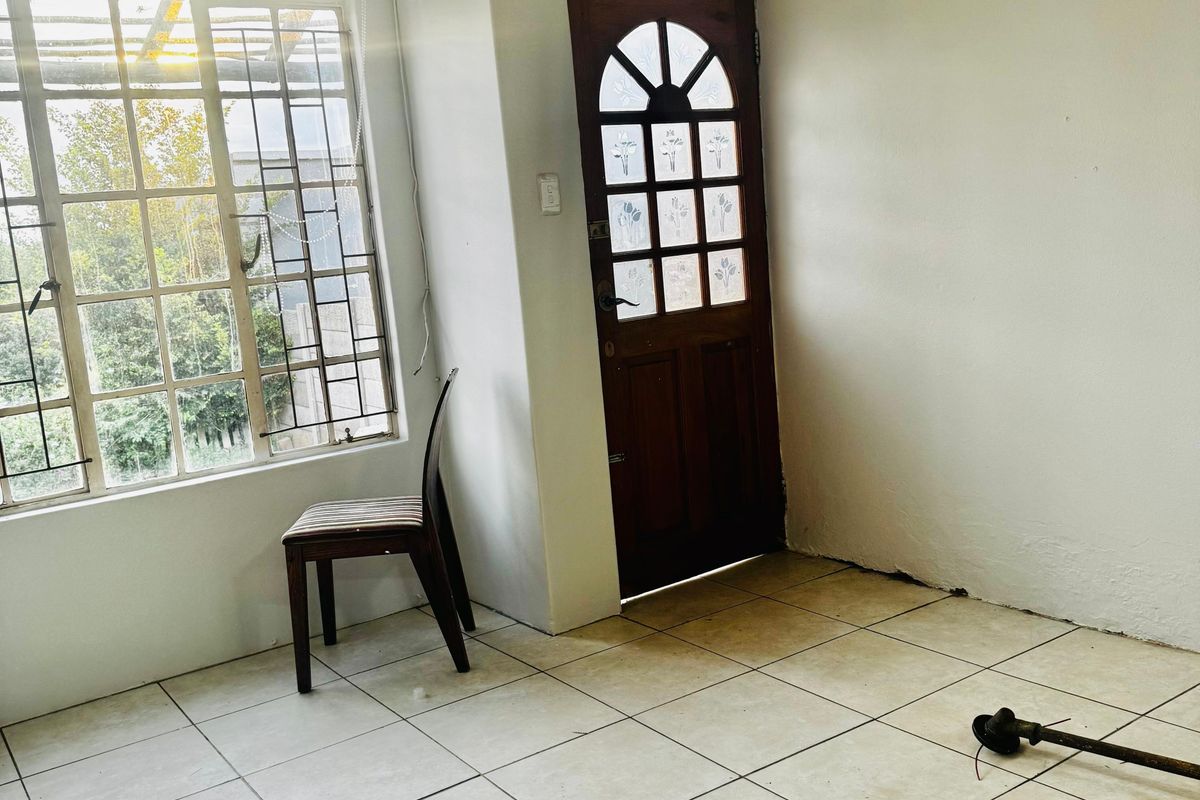 An empty living area featuring tiled flooring, a timber entrance door with decorative glass, and security bars on the window.