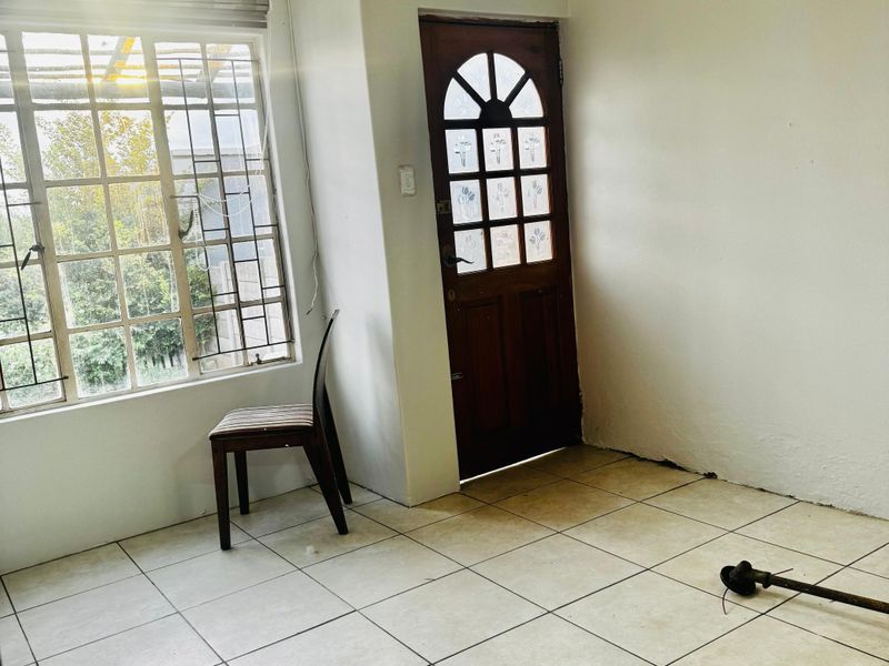 An empty living area featuring tiled flooring, a timber entrance door with decorative glass, and security bars on the window.