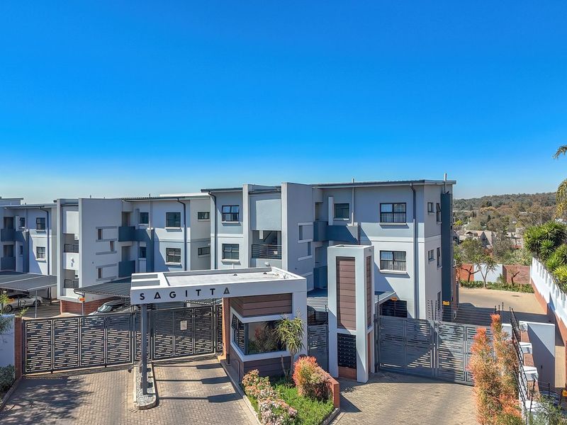 Aerial view of the Sagitta apartment complex entrance, featuring a secure gated access point, guard house, and paved driveway with covered parking bays.
