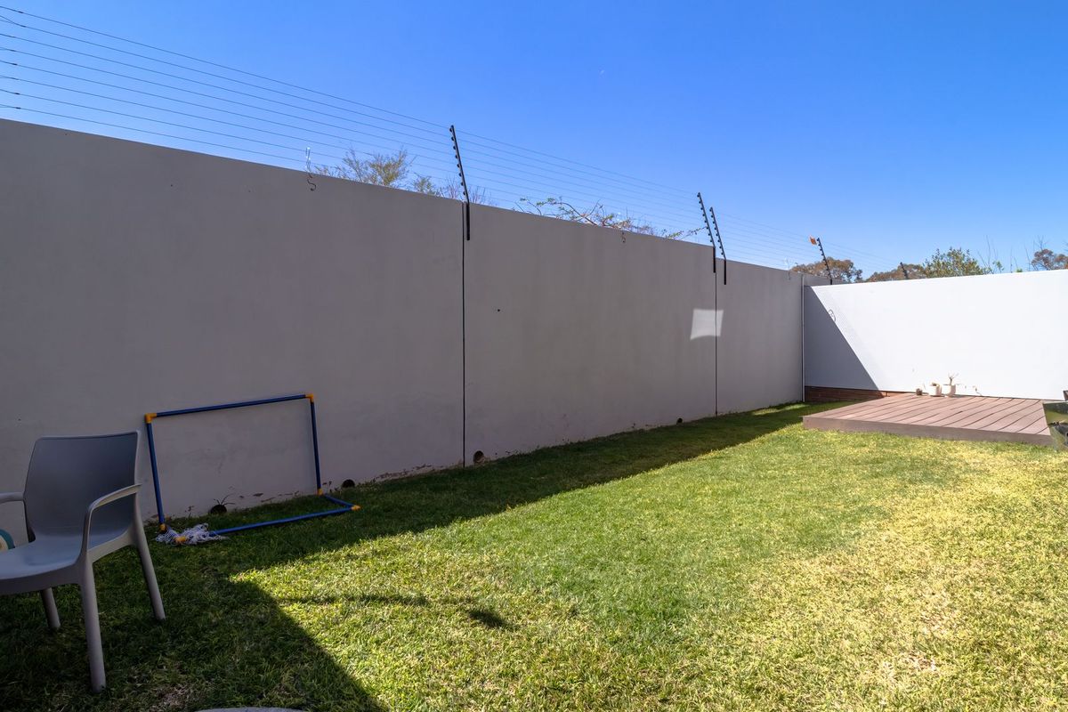 A private rear garden featuring a well-maintained lawn, timber decking area, and secure perimeter wall with installed electric fencing.