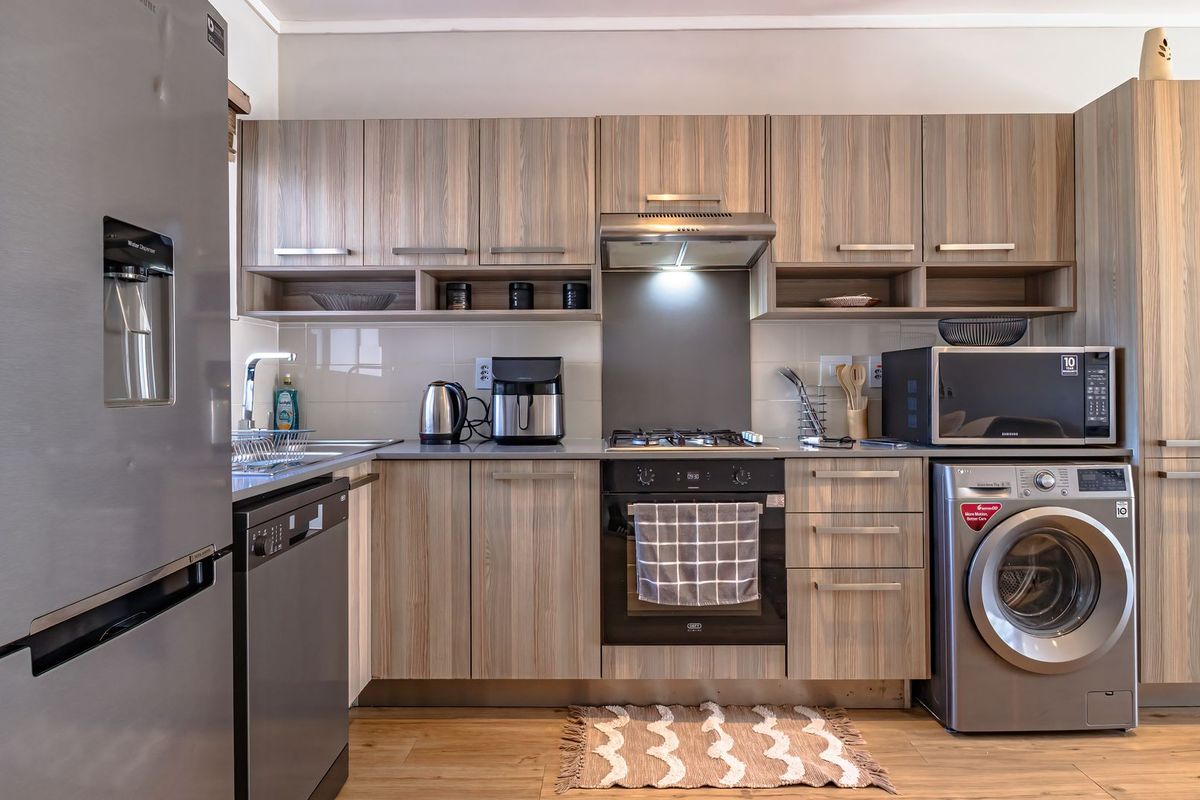 Modern kitchen featuring wood-grain cabinetry, integrated appliances, stainless steel oven and hob, and durable laminate flooring in a clean, functional layout.